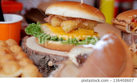 Gourmet sandwich with crispy toppings, Sunny festival stand serving elegant handcrafted burgers, Lively outdoor market offering gourmet burgers with melted cheese and crunchy vegetables on wooden 136408607