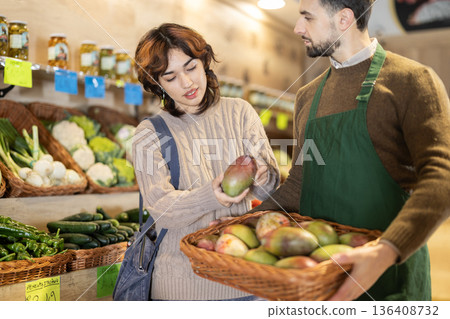 Young girl choosing mango from basket held by male seller grocery market Young girl choosing mango from basket held by male seller grocery market 136408732