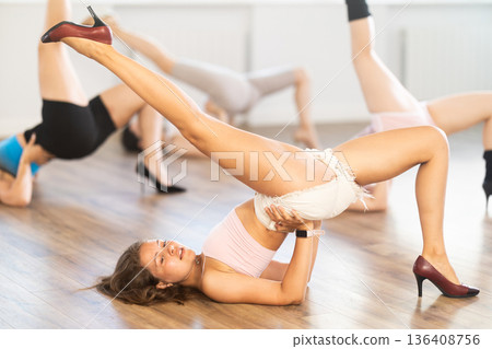 In choreographic studio, girls in high heels perform candid dance, move towards floor, pose on floor In choreographic studio, girls in high heels perform candid dance, move towards floor, pose on floor 136408756
