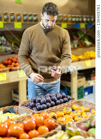 Man near vegetable stand in store choose plum. Man near vegetable stand in store choose plum. 136408761