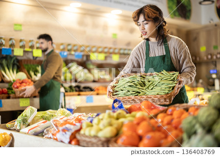 Young female seller holding basket of string beans in grocery market 136408769