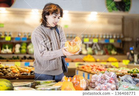 Female shopper selects ripe pumpkin at grocery store 136408771