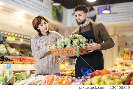 Young girl choosing artichoke from basket held by male seller grocery market Young girl choosing artichoke from basket held by male seller grocery market 136408839