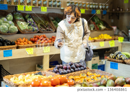 Young woman chooses plums in store 136408861