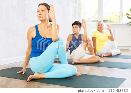 Mother, grandmother and adolescence son do exercise lord of fish, Ardha Matsyedrasana Mother, grandmother and adolescence son do exercise lord of fish, Ardha Matsyedrasana 136408883