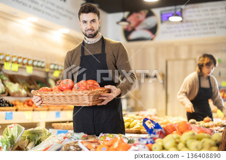 Man employees in uniform carries wicker basket with tomatoes in grocery shop 136408890