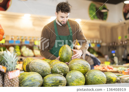 Man seller in grocery vegetable shop arrange melon. Man seller in grocery vegetable shop arrange melon. 136408919