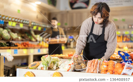 Young female seller putting kiwis on counter in grocery market Young female seller putting kiwis on counter in grocery market 136408937