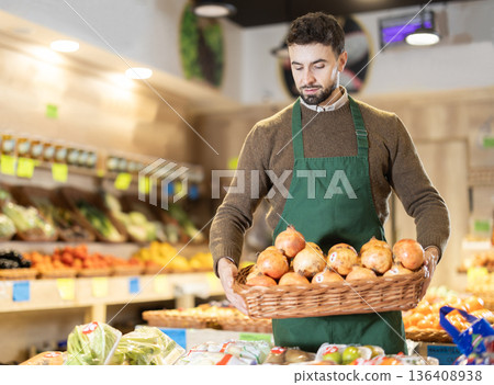 Young male seller holding basket of pomegranates in grocery market 136408938
