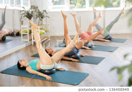 Together with students, teacher lies with fitball under her buttocks and performs swings with feet Together with students, teacher lies with fitball under her buttocks and performs swings with feet 136408949