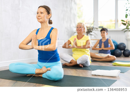 Middle-aged woman practicing easy pose of yoga in light fitness room Middle-aged woman practicing easy pose of yoga in light fitness room 136408953