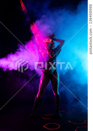 Futuristic woman in glowing glasses dancing with light stick in pink and blue neon smoke. Futuristic woman in glowing glasses dancing with light stick in pink and blue neon smoke. 136408998