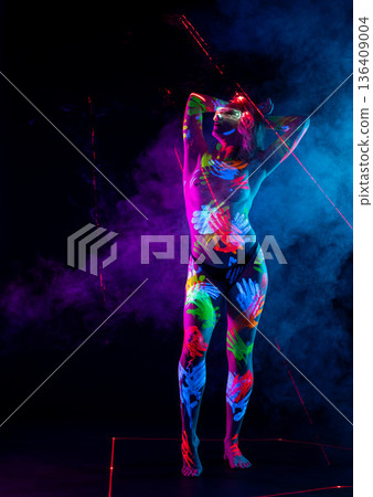 Futuristic woman with neon body art handprints and glowing glasses in blacklight studio. Futuristic woman with neon body art handprints and glowing glasses in blacklight studio. 136409004