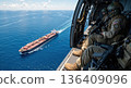 Soldiers in helicopter patrolling over cargo ship in ocean. Military maritime security operation aerial view 136409096