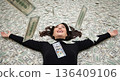Top view of a happy woman lying on a bed of money. Successful female winner with falling dollars. Wealth and financial freedom concept 136409106