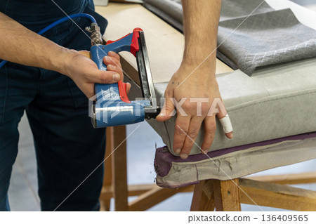 Worker's hand operates a blue pneumatic stapler. Worker's hand operates a blue pneumatic stapler. 136409565
