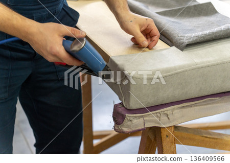 Worker's hand operates a blue pneumatic stapler. 136409566