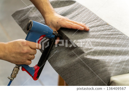 Worker's hand operates a blue pneumatic stapler. 136409567