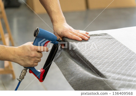 Worker's hand operates a blue pneumatic stapler. Worker's hand operates a blue pneumatic stapler. 136409568