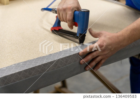 Worker's hand operates a blue pneumatic stapler. Worker's hand operates a blue pneumatic stapler. 136409583