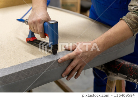 Worker's hand operates a blue pneumatic stapler. Worker's hand operates a blue pneumatic stapler. 136409584