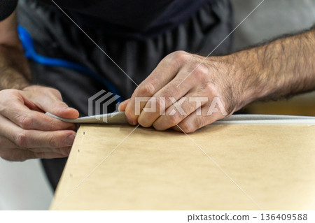 Close-up of craftsman hands stretching upholstery fabric over wooden furniture frame Close-up of craftsman hands stretching upholstery fabric over wooden furniture frame 136409588
