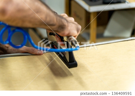 Close-up of upholsterer using a pneumatic staple gun to attach fabric to a wooden furniture frame. 136409591