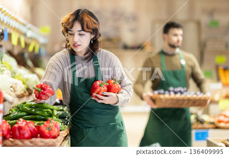 Young woman seller puts peppers in store Young woman seller puts peppers in store 136409995