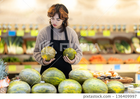 Woman employees in uniform holding pumpkin in grocery shop 136409997