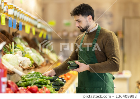 Male seller in uniform working in supermarket, checking cucumber 136409998