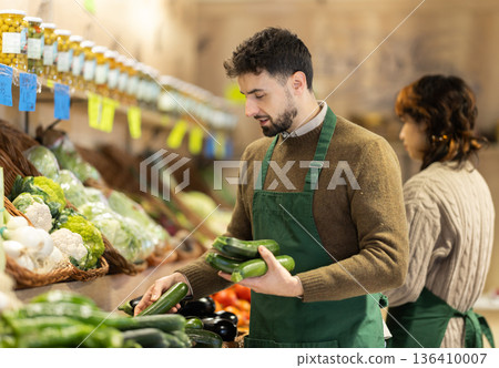 Man seller in grocery vegetable shop with zucchini Man seller in grocery vegetable shop with zucchini 136410007