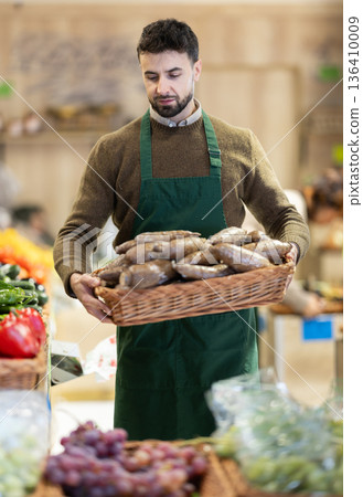 Man seller in grocery vegetable shop with yucca root. Man seller in grocery vegetable shop with yucca root. 136410009