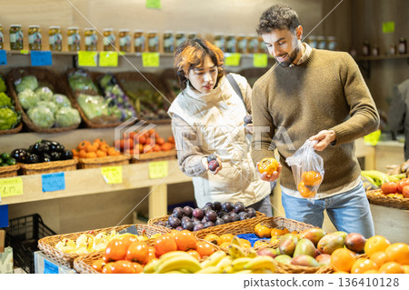 Couple shopping in vegetable store and buy elect fruits plum and persimmon. 136410128