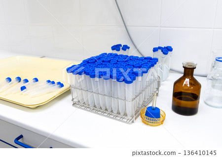 Laboratory sample tubes with blue caps in rack and glass reagent bottle on workbench Laboratory sample tubes with blue caps in rack and glass reagent bottle on workbench 136410145