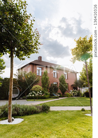 Brick family house with landscaped backyard, green lawn, trees and patio in sunlight 136410316