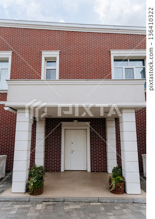 Front entrance of modern brick house with white columns, porch and closed door 136410322
