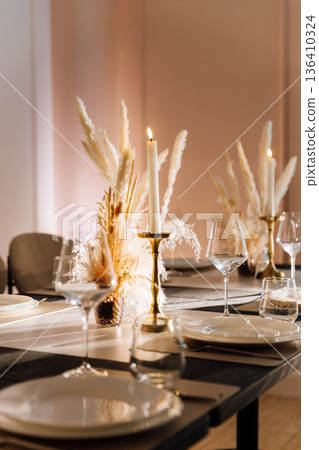 Candlelit restaurant table setting with pampas centerpiece and warm evening ambiance Candlelit restaurant table setting with pampas centerpiece and warm evening ambiance 136410324