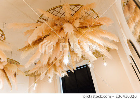 Boho pampas grass ceiling installation with warm pendant lights in modern interior Boho pampas grass ceiling installation with warm pendant lights in modern interior 136410326