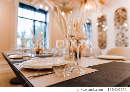Elegant restaurant table setting with glassware, pampas decor and warm bokeh lighting Elegant restaurant table setting with glassware, pampas decor and warm bokeh lighting 136410331