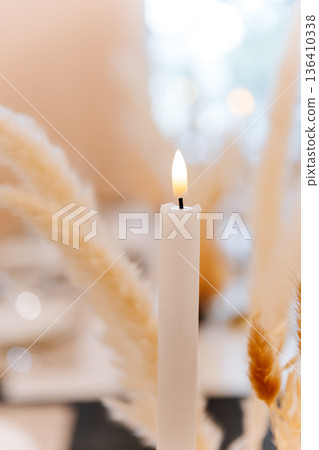 Lit white candle with soft bokeh in elegant neutral dining decor, cozy atmosphere Lit white candle with soft bokeh in elegant neutral dining decor, cozy atmosphere 136410338