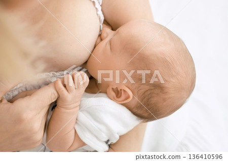 Close-up of breastfeeding newborn baby in mother arms on light background. Natural feeding, maternal care, baby health, bonding, early childhood and healthy development concept. Close-up of breastfeeding newborn baby in mother arms on light background. Natural feeding, maternal care, baby health, bonding, early childhood and healthy development concept. 136410596