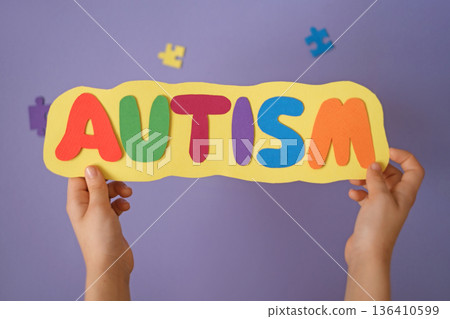 Colorful paper letters spelling autism in child hands. Autism awareness, inclusive education, social support, early learning and childhood development concept. 136410599