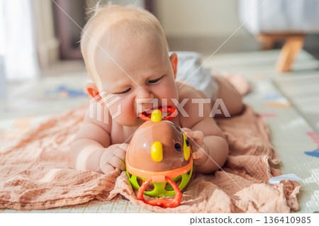 Little baby playing with toys on a soft baby play mat at home. Early childhood development, sensory play, learning through play, curiosity, and happy infant activity concept for modern parenting. 136410985