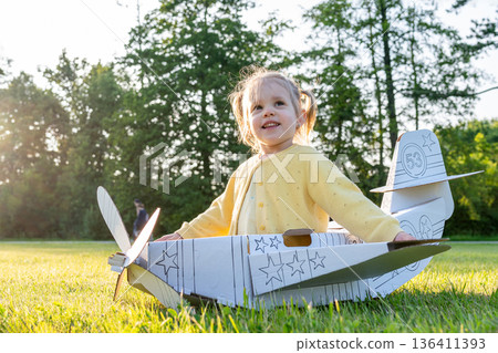Child with airplane. Girl cardboard pilot toy. Imagination outdoor costume summer. Child with airplane. Girl cardboard pilot toy. Imagination outdoor costume summer. 136411393