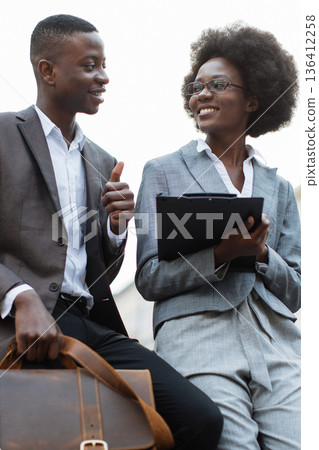 Colleagues consult a clipboard outdoors between meetings, conveying collaboration and professional confidence for corporate use in editorial contexts 136412258