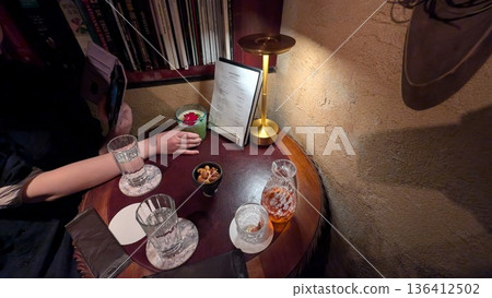 一位女士在一家氛圍輕鬆的酒吧里，坐在桌旁享用飲品。 136412502