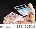 Business image of a stack of bills, a calculator, and a wooden doll 136412514