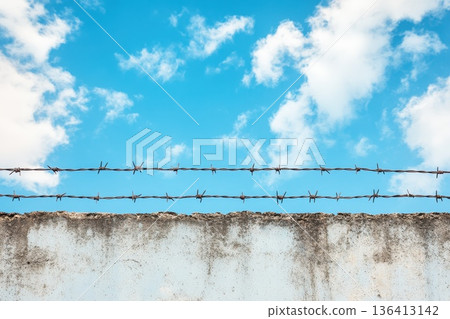 Blue Sky with Barbed Wire on Top of Concrete Wall against a Backdrop of Clouds 136413142