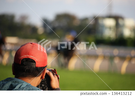 A man taking pictures of a race at a racetrack, rear view of a camera and telephoto lens 136413212