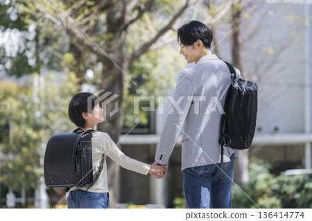 一個三年級男孩和他三十多歲的父親手牽手散步。 一個三年級男孩和他三十多歲的父親手牽手散步。 136414774